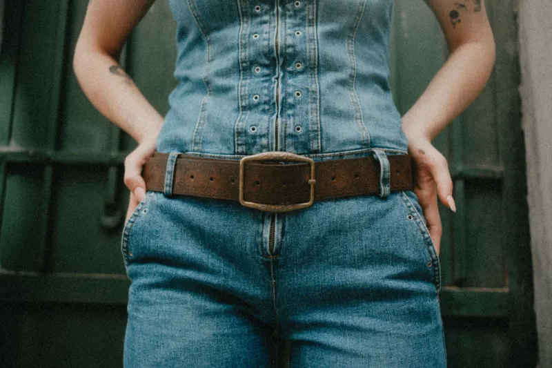 Brown leather belt with a brass buckle worn over a denim jumpsuit