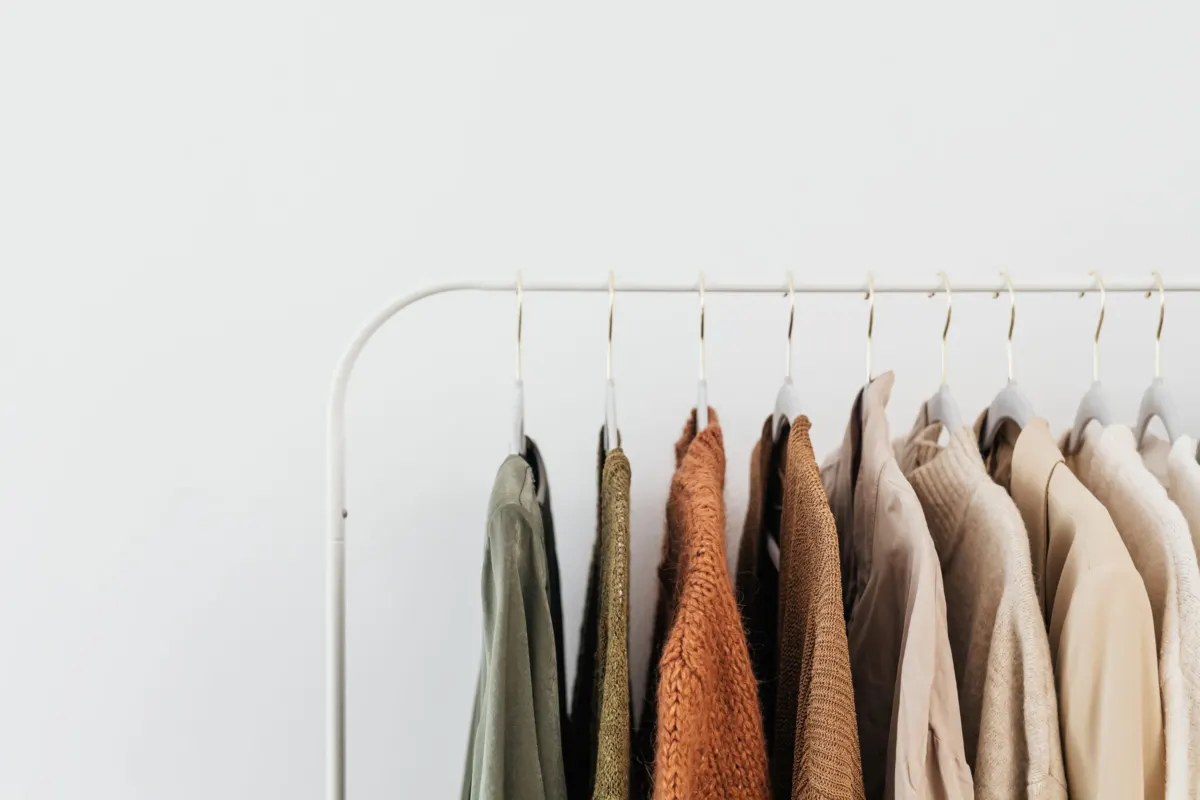 Clothes rail with shirts and jackets in olive, rust, beige and cream against a white wall