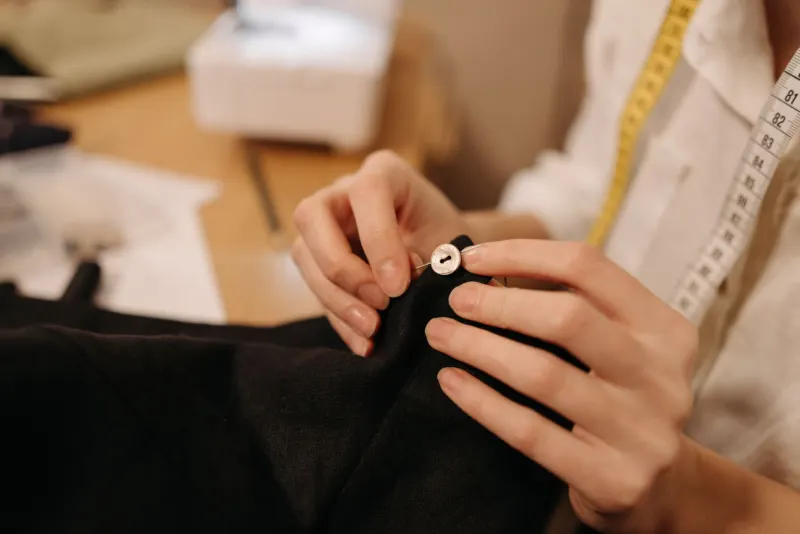 Hands sewing a button onto a black garment