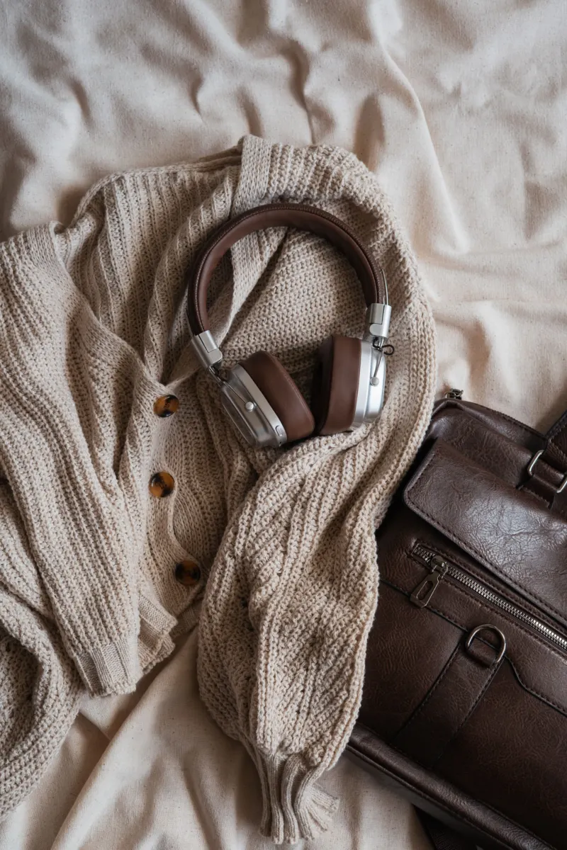Cream cable-knit cardigan, brown leather bag and headphones on a linen sheet