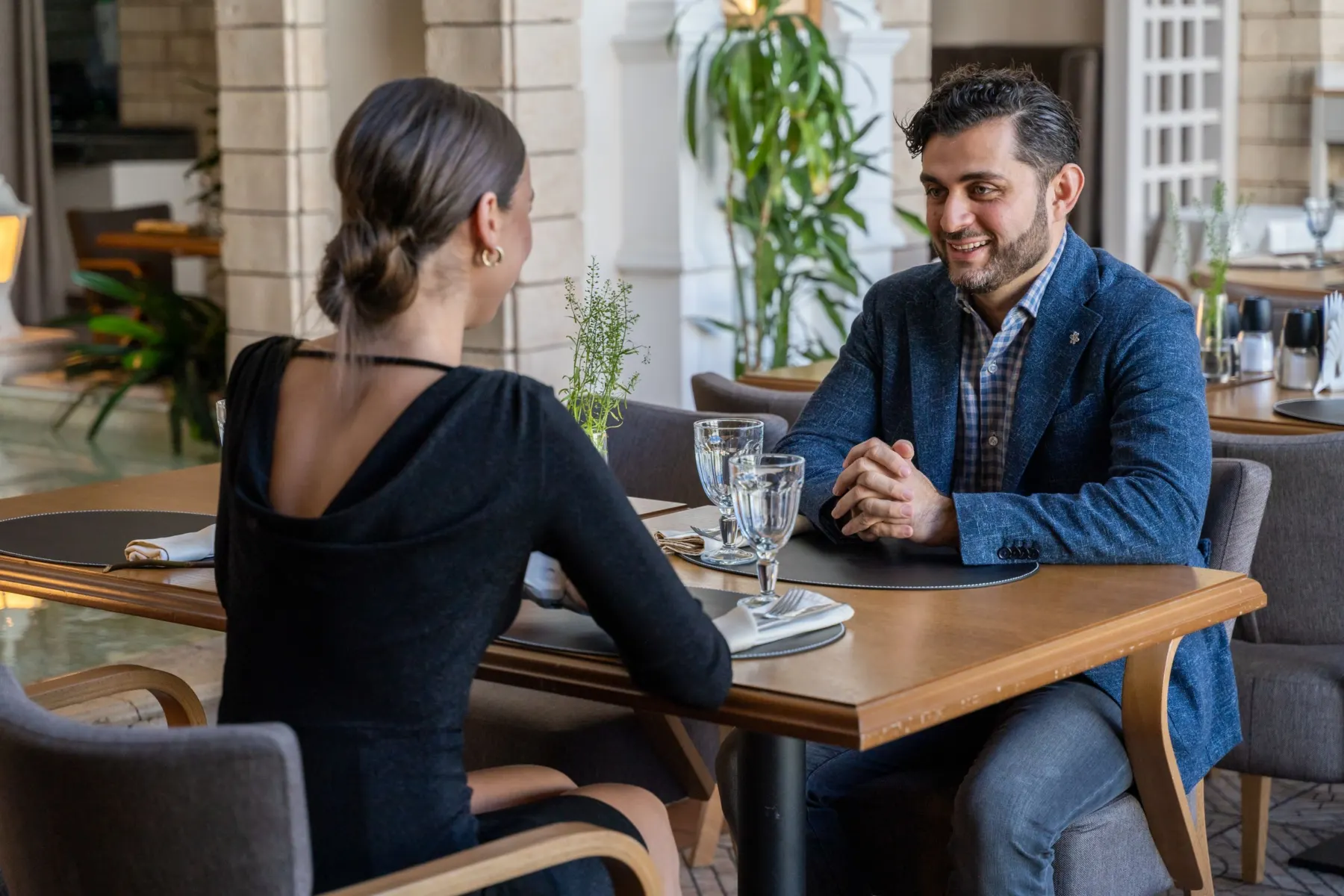 Two people in a blue blazer and a black dress talking at a restaurant table