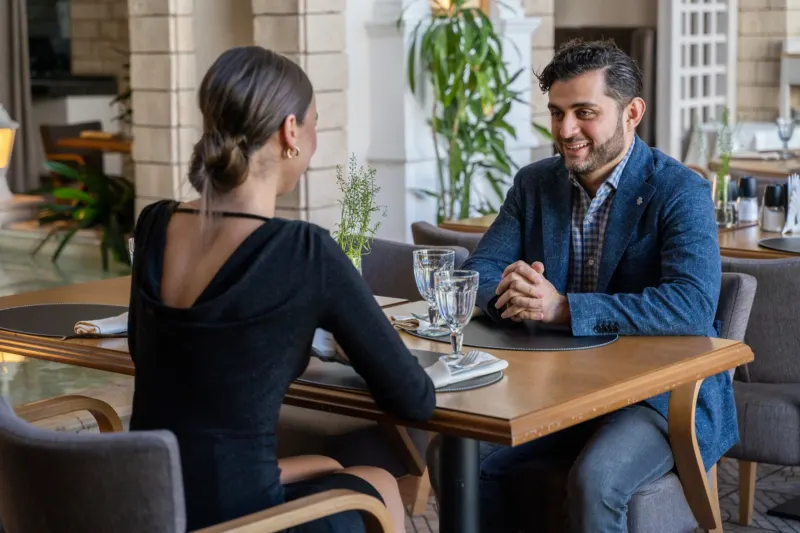 Two people in a blue blazer and a black dress talking at a restaurant table