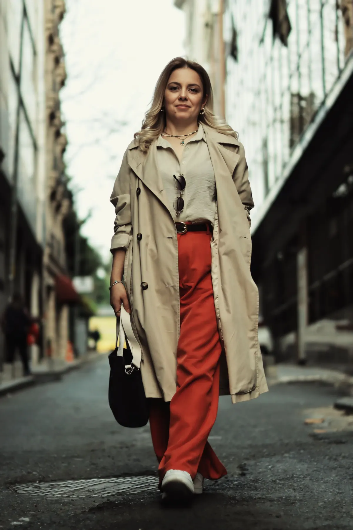 Woman in a trench coat and red trousers walking down a street