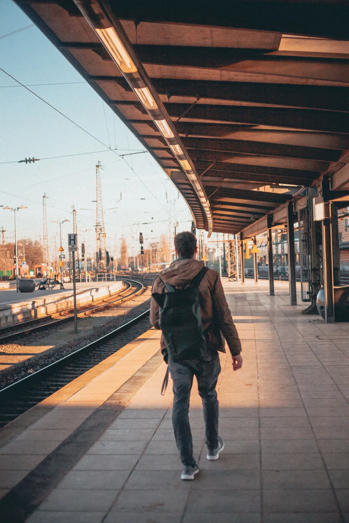 Traveller with a backpack walking along a station platform at sunset