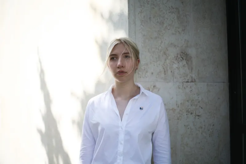 Woman in a white shirt standing in soft daylight by a stone wall