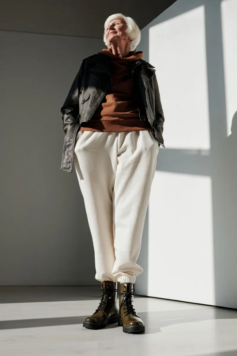 Older woman in a leather jacket, cream trousers and lace-up boots standing in sunlight
