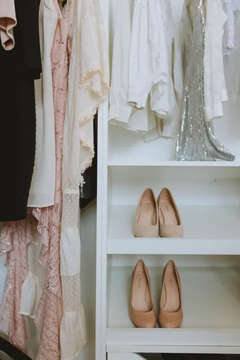 Wardrobe with pale dresses hanging beside shelves holding two pairs of shoes