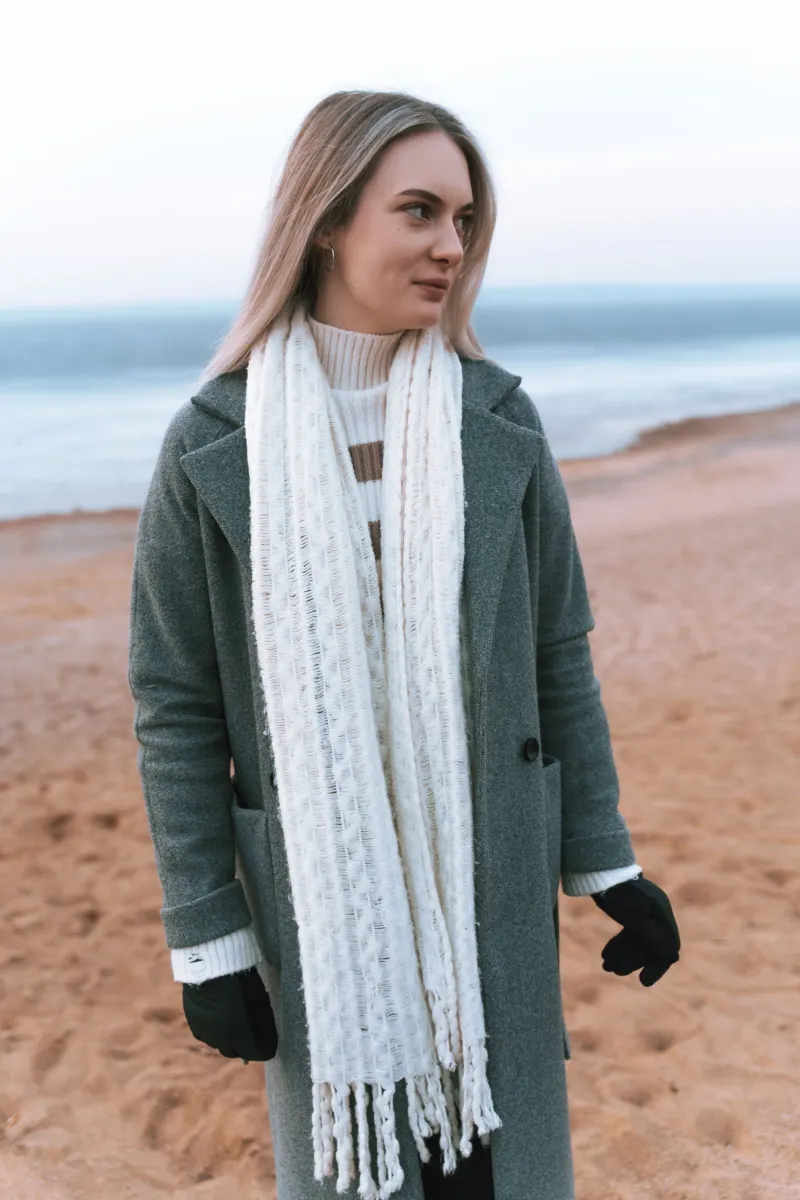 Woman on a beach in a green coat with a long white knitted scarf