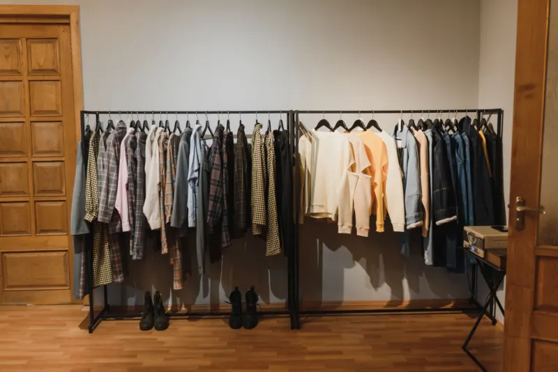 Two clothes rails full of jackets and shirts in a room with a wooden floor