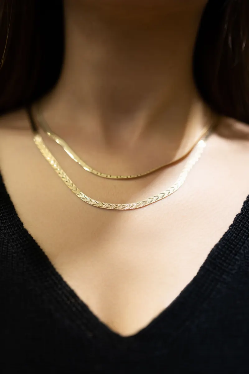 Two gold chain necklaces worn with a black V-neck top