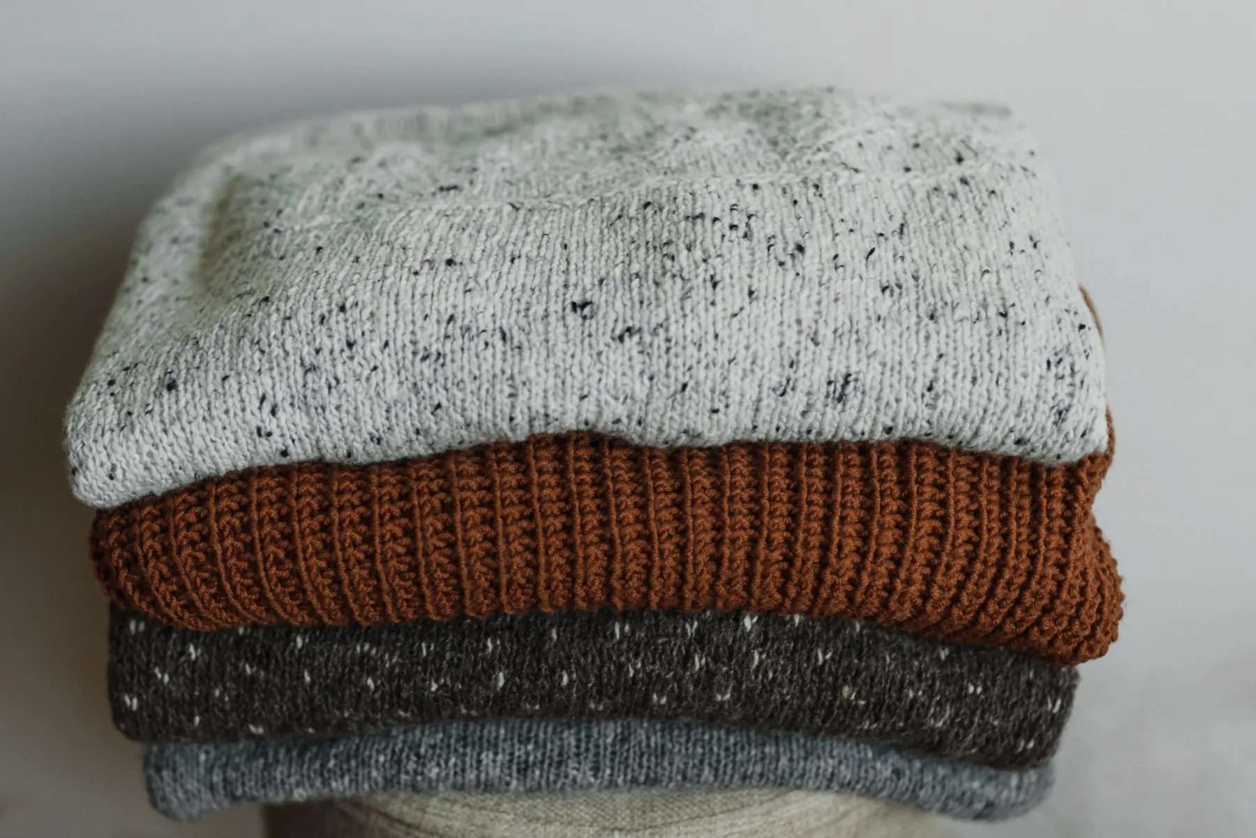 Stack of four folded jumpers in grey, rust and charcoal