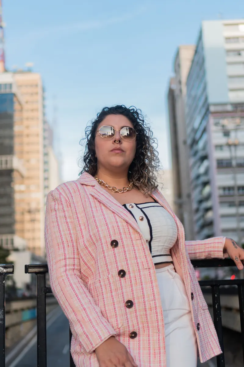 Woman in a pink checked blazer and white trousers on a city balcony