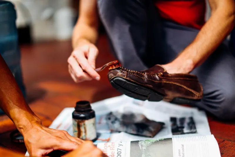 Hands brushing a brown leather shoe over newspaper