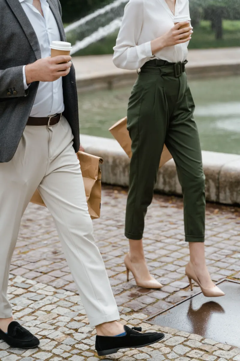 Two people walking: cream trousers with black loafers, green trousers with pale heels