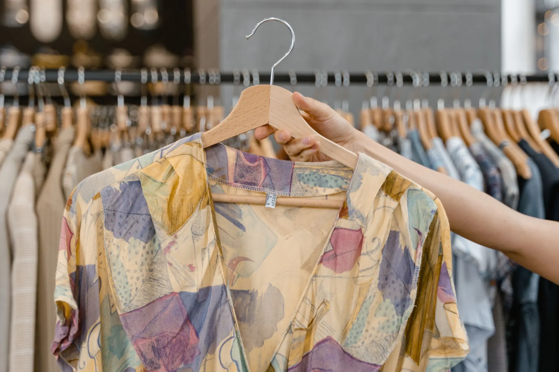 Hand lifting a patterned shirt on a hanger from a rail of second-hand clothes