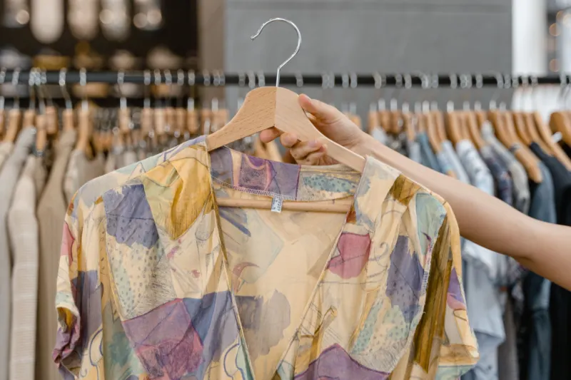 Hand lifting a patterned shirt on a hanger from a rail of second-hand clothes
