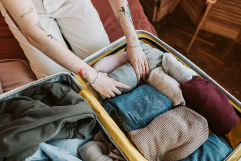 Hands packing folded jumpers and jeans into an open suitcase
