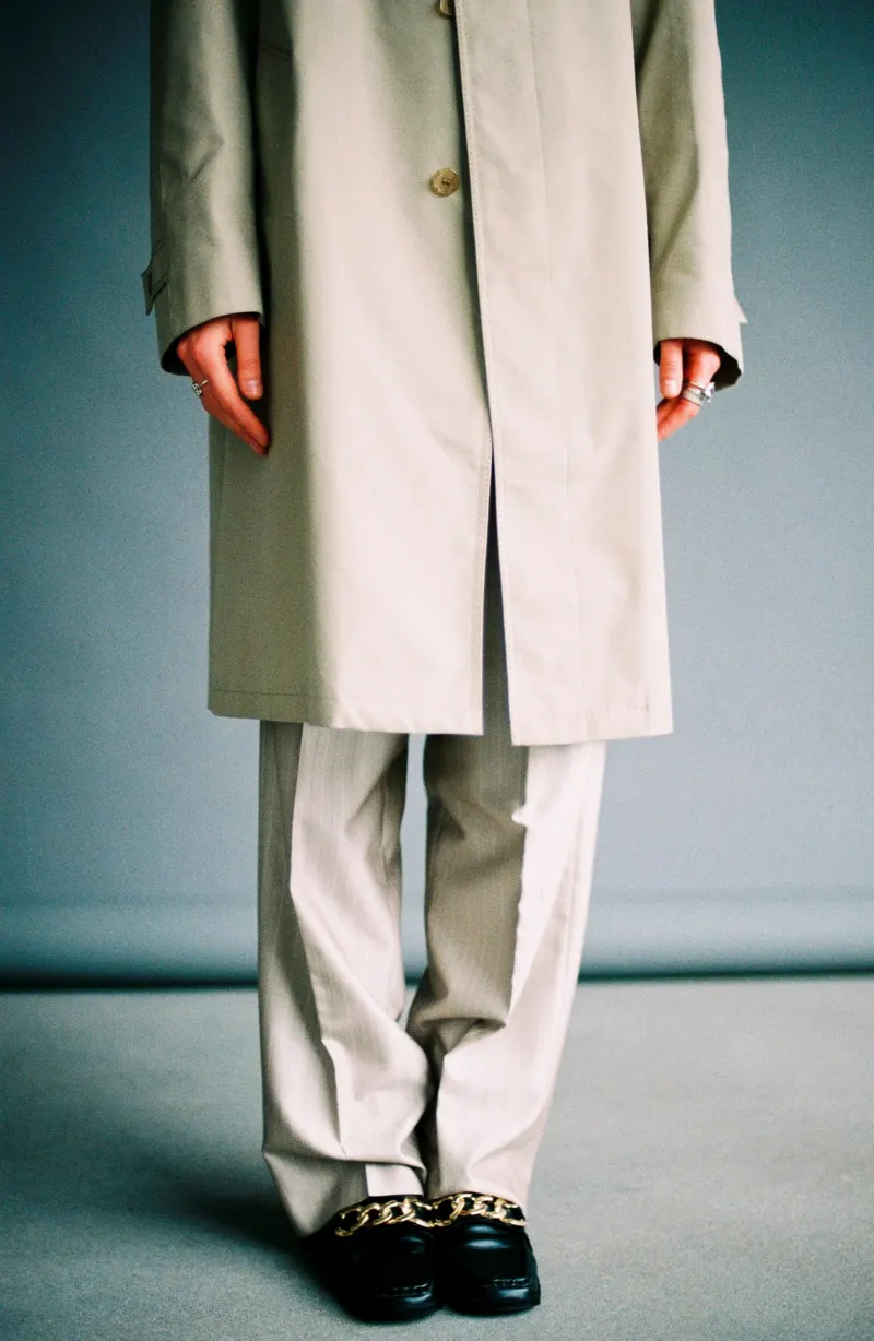 Long pale coat over wide cream trousers and black loafers, shown from the shoulders down