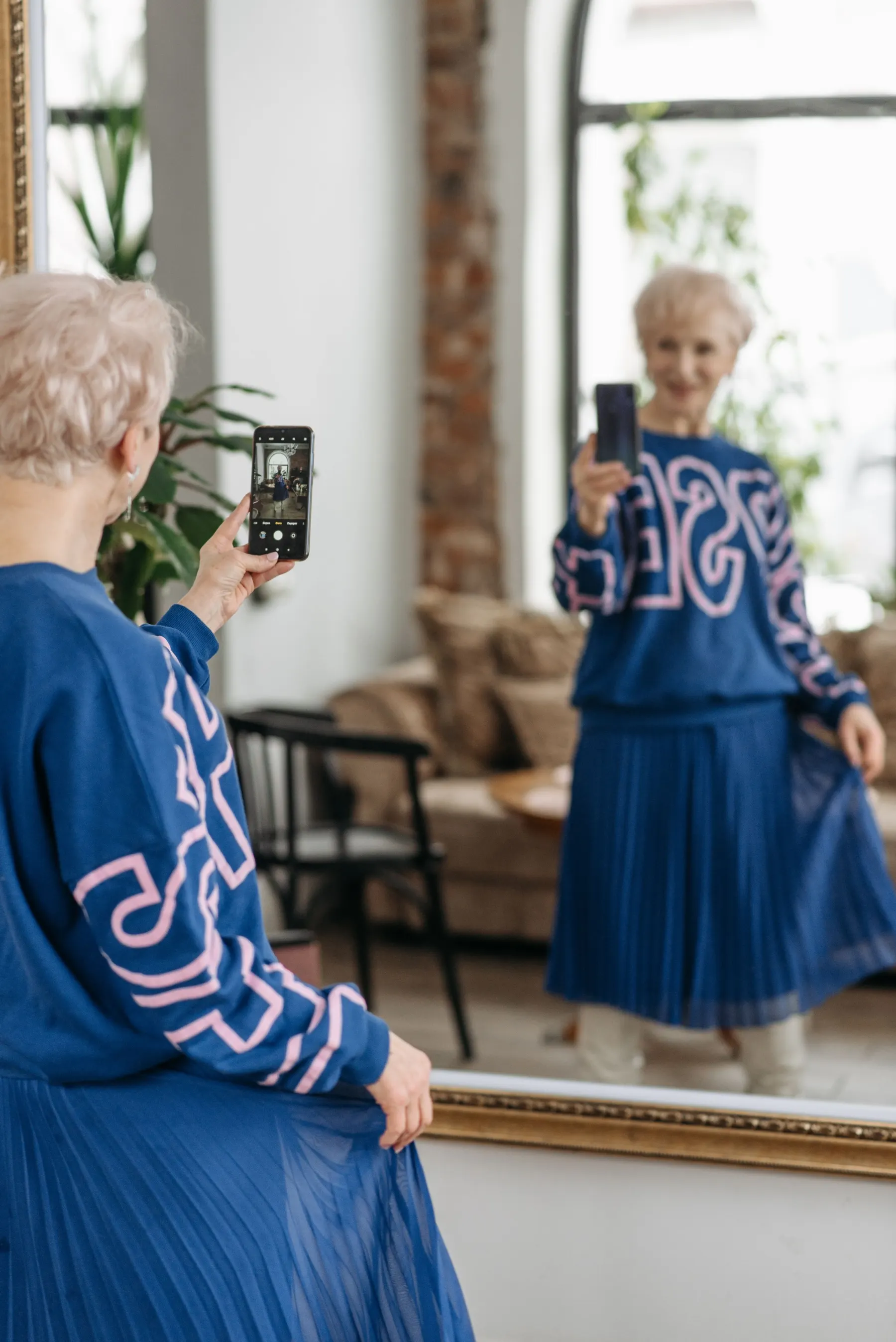 Older woman in a blue patterned outfit photographing herself in a mirror