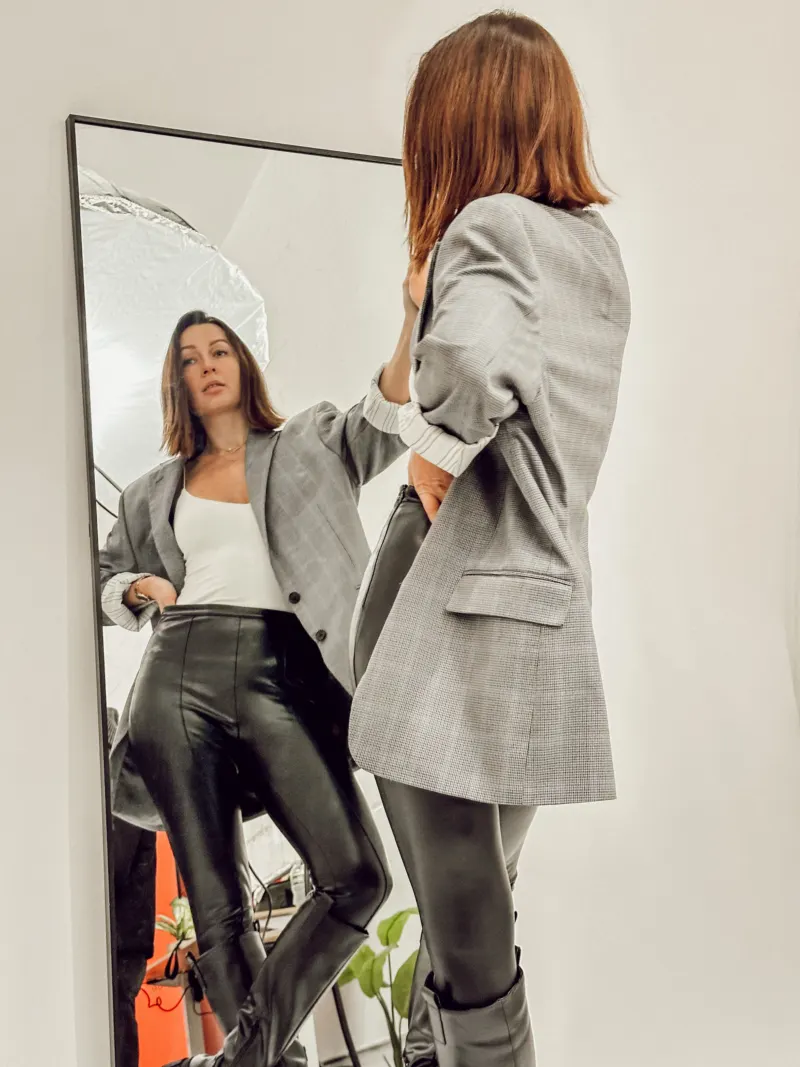 Woman checking the fit of a grey checked blazer in a full-length mirror